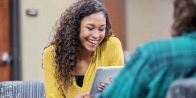 A woman is smiling while looking at a tablet computer.