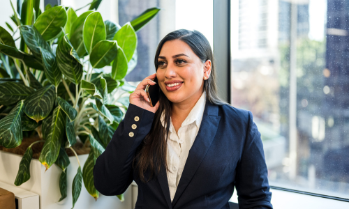 A woman in a suit is talking on a cell phone in front of a window.