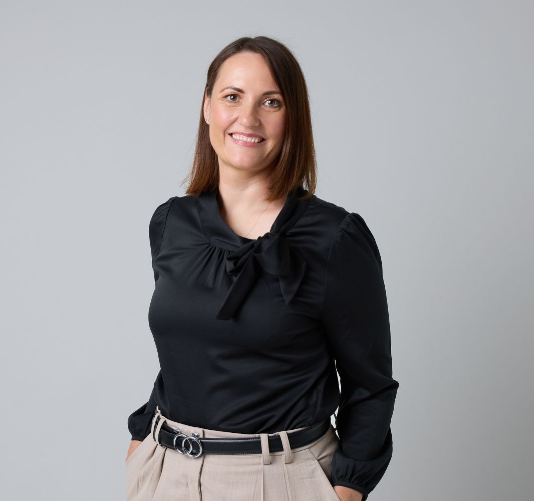 A woman in a black top is smiling with her hands in her pockets.