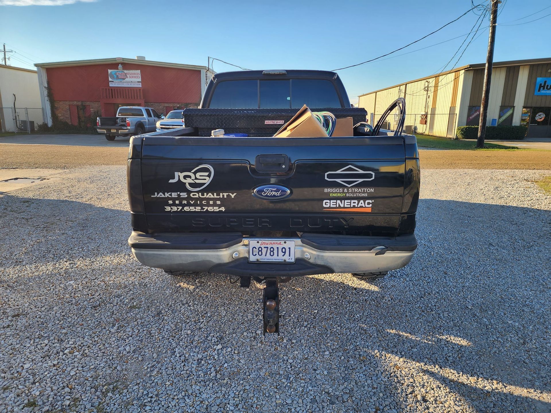 Black pickup truck with decals parked on gravel in front of industrial buildings, rear view