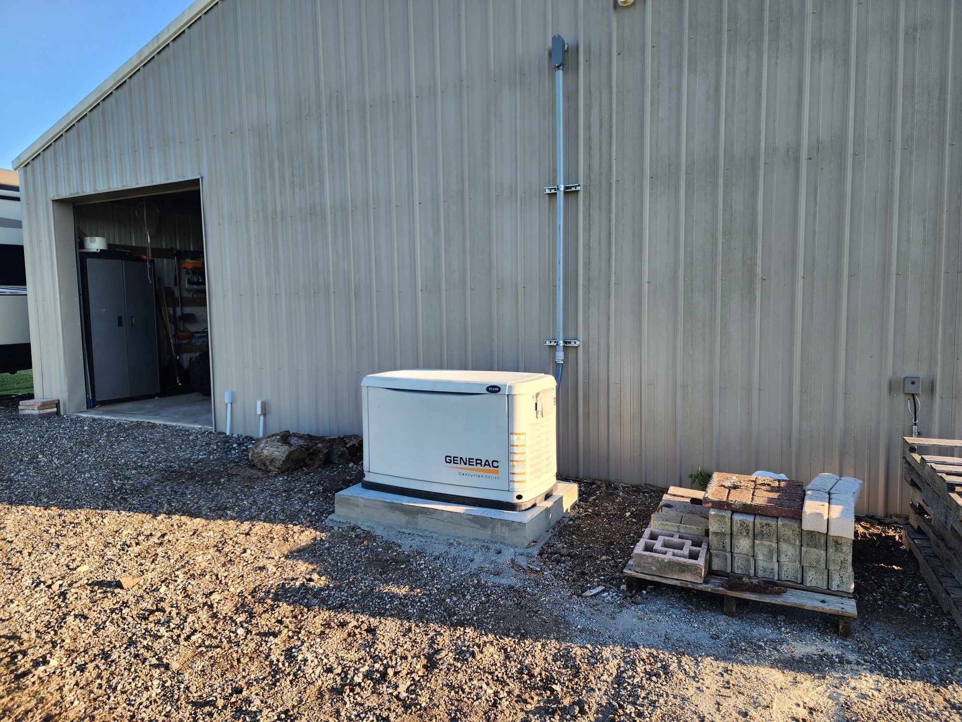 Outdoor generator beside a metal building with pallets and gravel ground