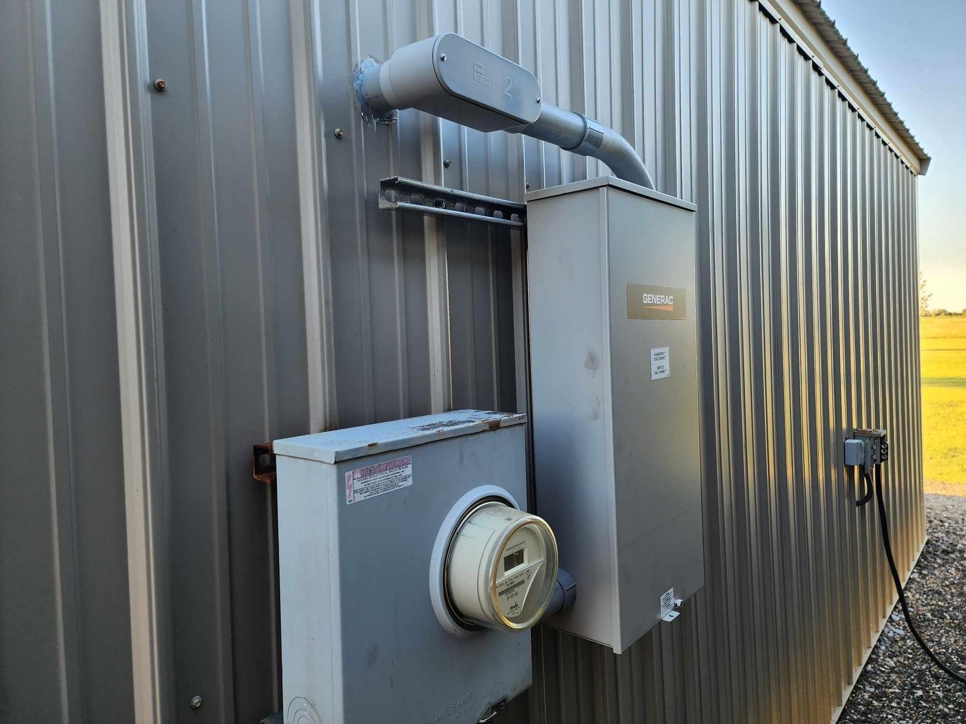 Electrical meter and gray utility boxes mounted on a corrugated metal building exterior.