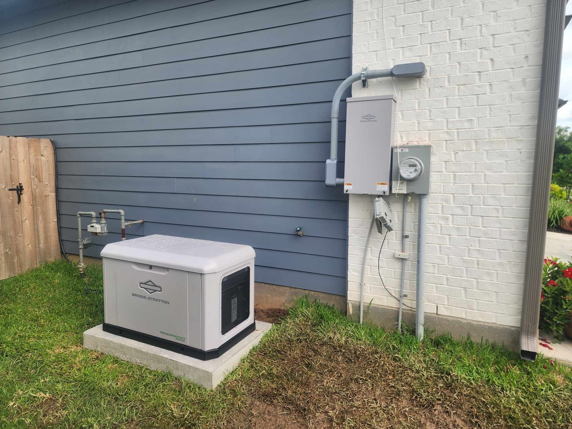 Outdoor backup generator beside a house with gray siding and electrical panels on the wall