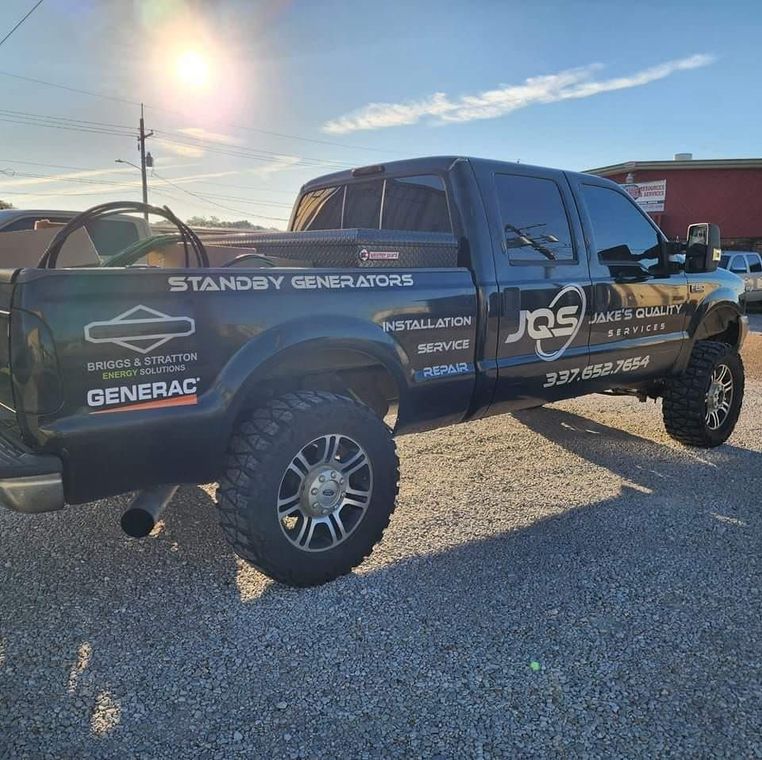 Black off-road pickup truck with sponsor decals parked on gravel in bright sunlight.
