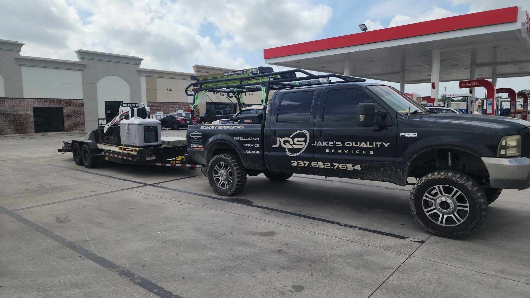 Black tow truck hauling a white vehicle at a gas station under a red canopy
