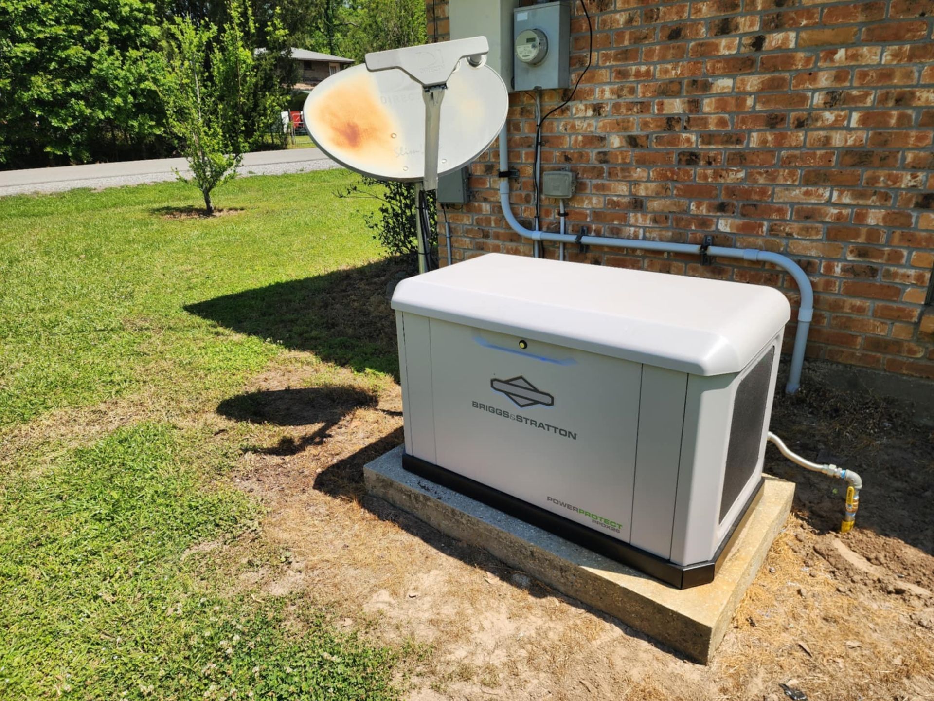 White outdoor generator beside brick house with satellite dish on grassy lawn