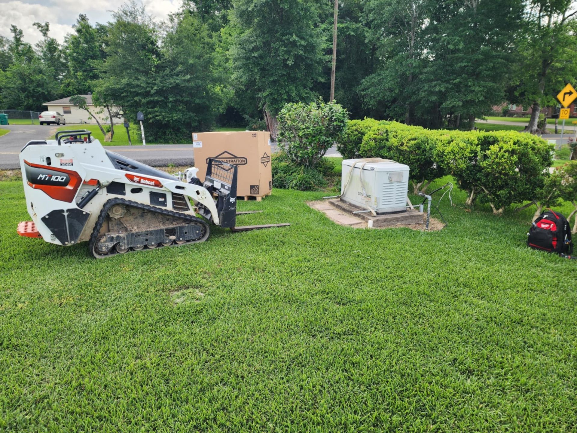 White Bobcat skid steer on grass beside utility boxes and a cardboard animal cutout in a yard