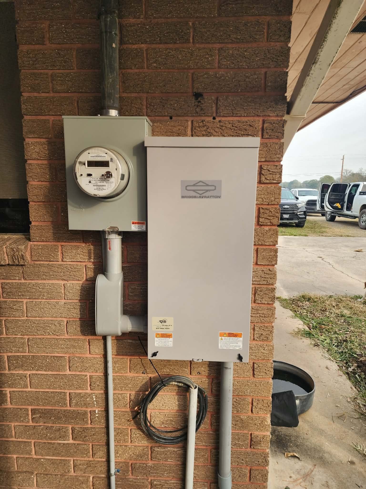 Electrical meter and utility box mounted on a brick wall beside a parking area.