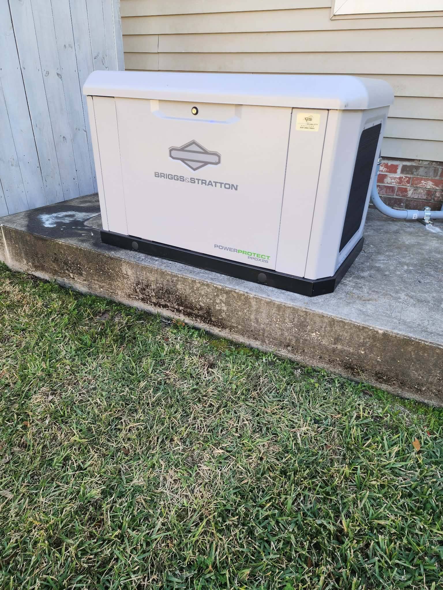 White generator on concrete slab beside house and grass, with power cord and small outdoor unit nearby