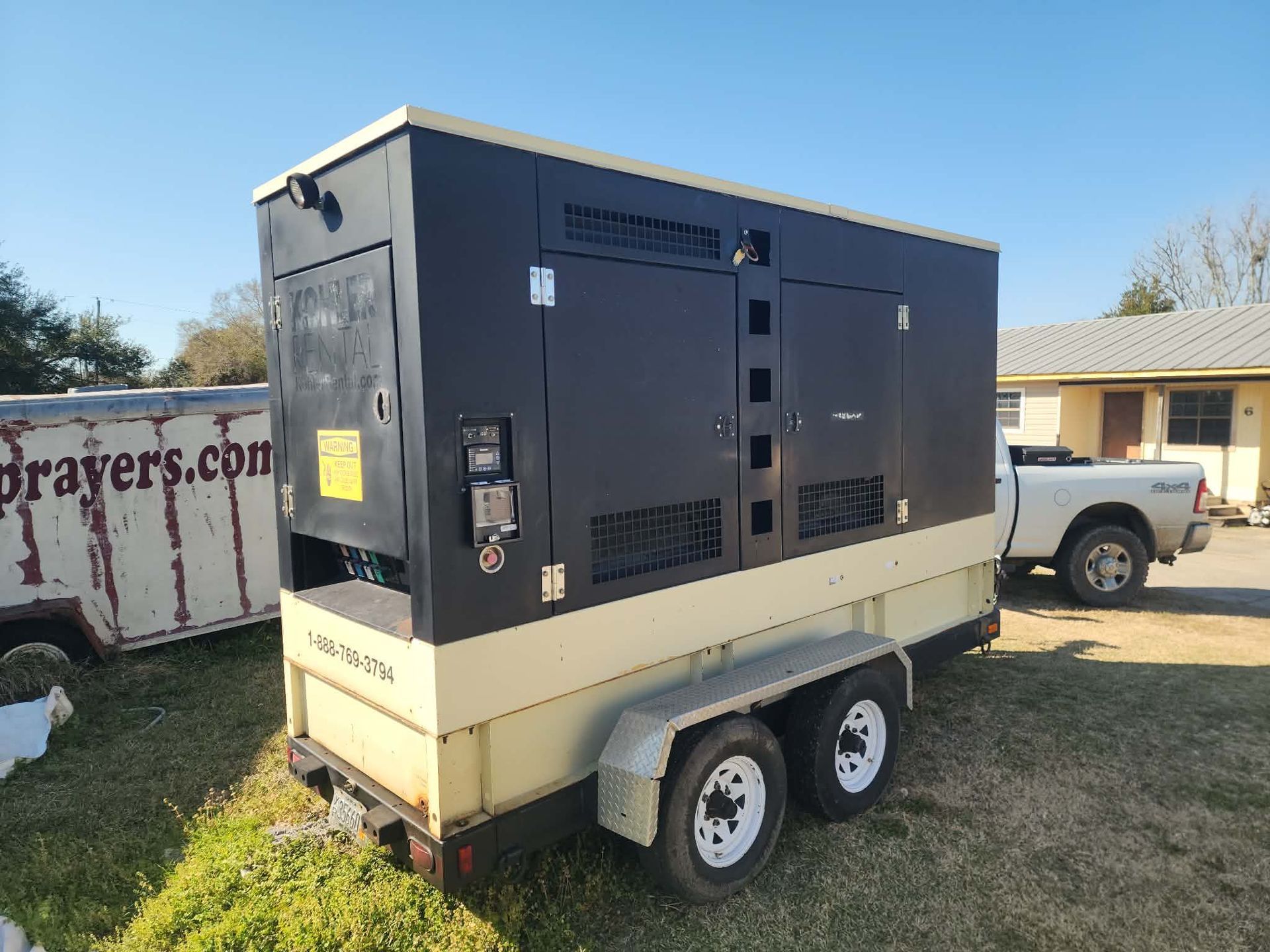 Portable generator mounted on a trailer in a grassy yard, with a pickup truck nearby.