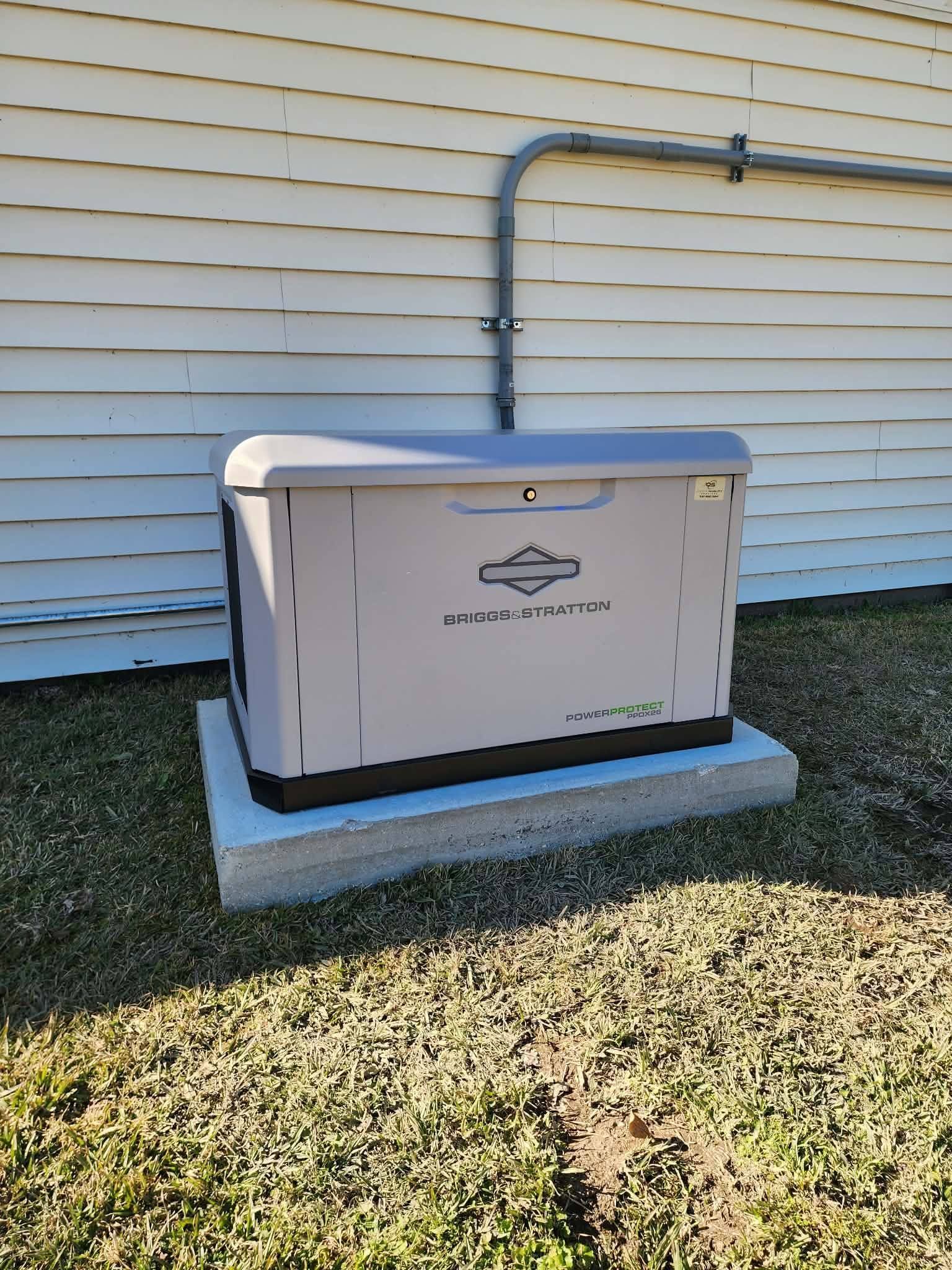 White standby generator on concrete pad beside beige house with gas line and conduit.