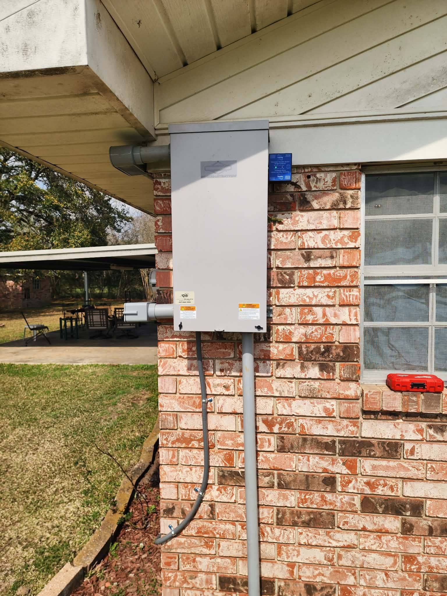 White utility box mounted on a brick wall under a roof eave, with conduit and cables attached