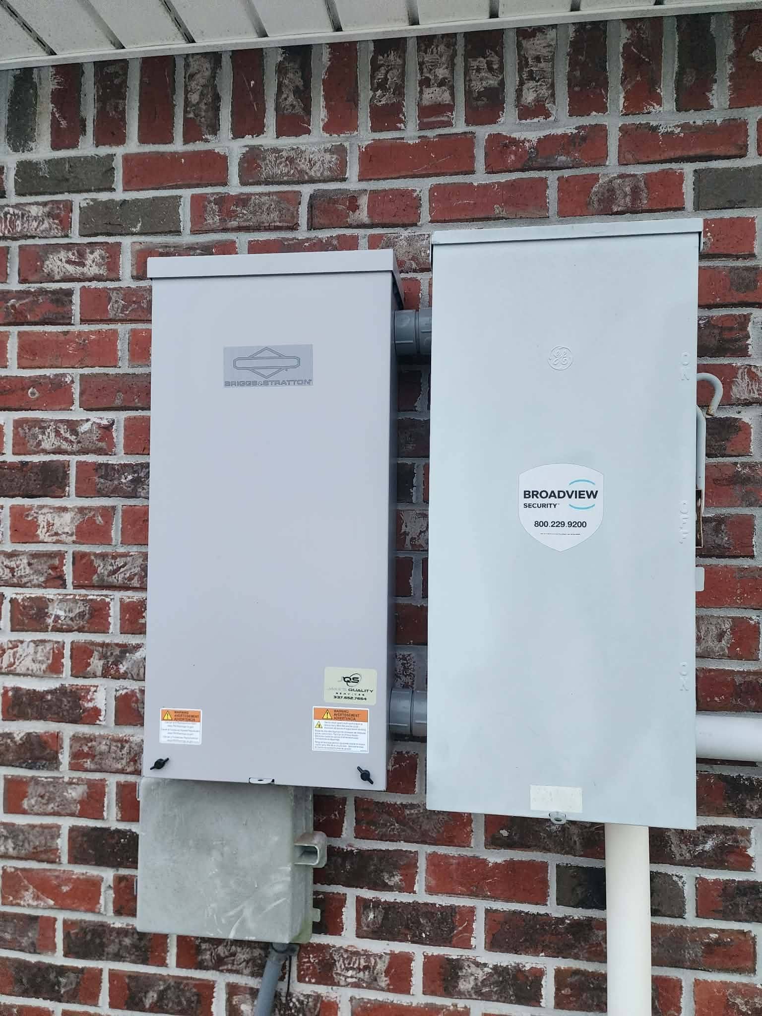 Two gray electrical utility boxes mounted on a red brick wall outdoors.