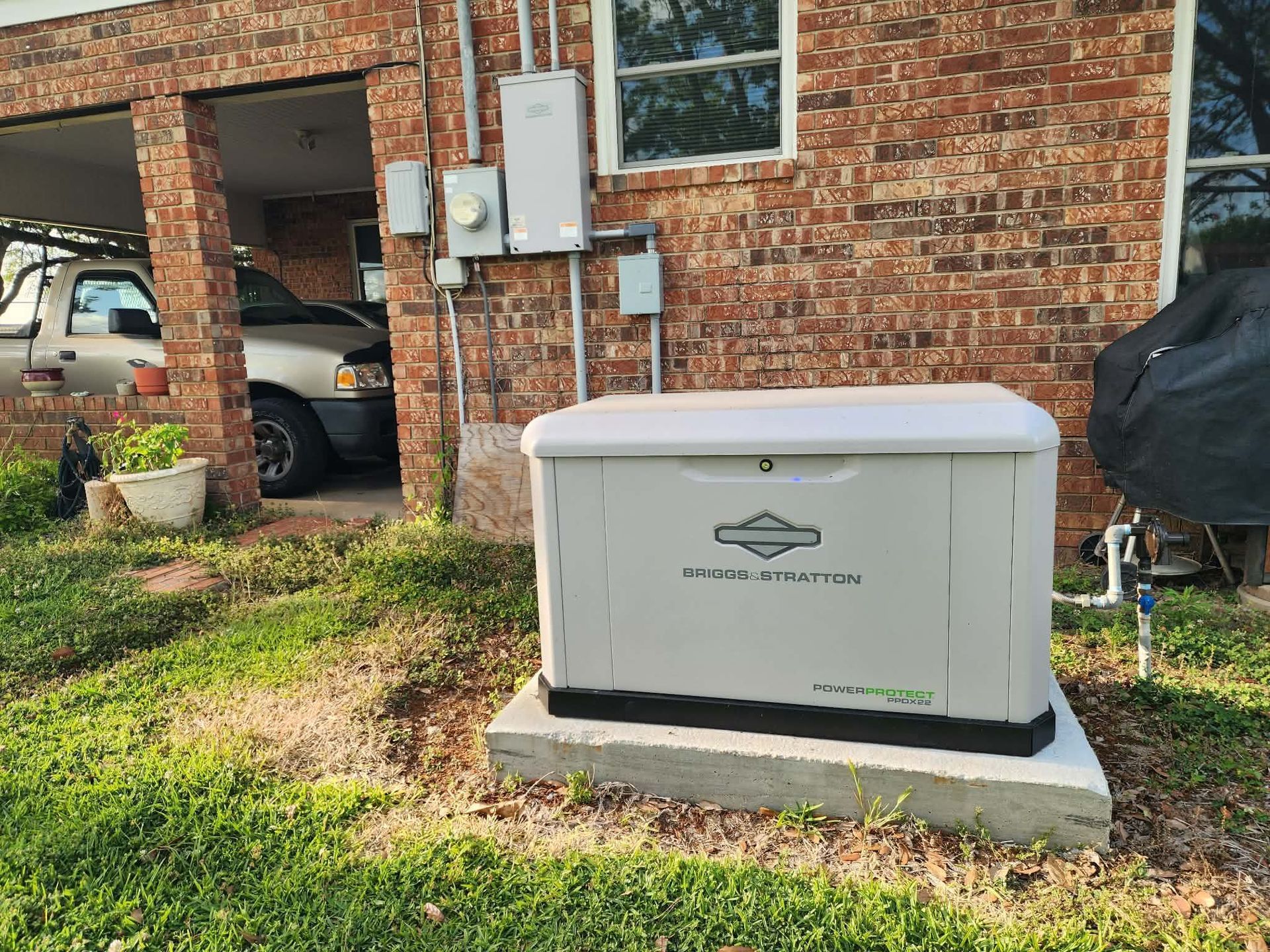 White generator on concrete pad beside a brick house with an open garage and parked car