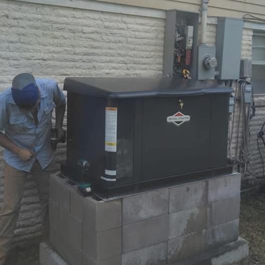 Technician inspects a rooftop HVAC unit beside a brick wall and concrete blocks.