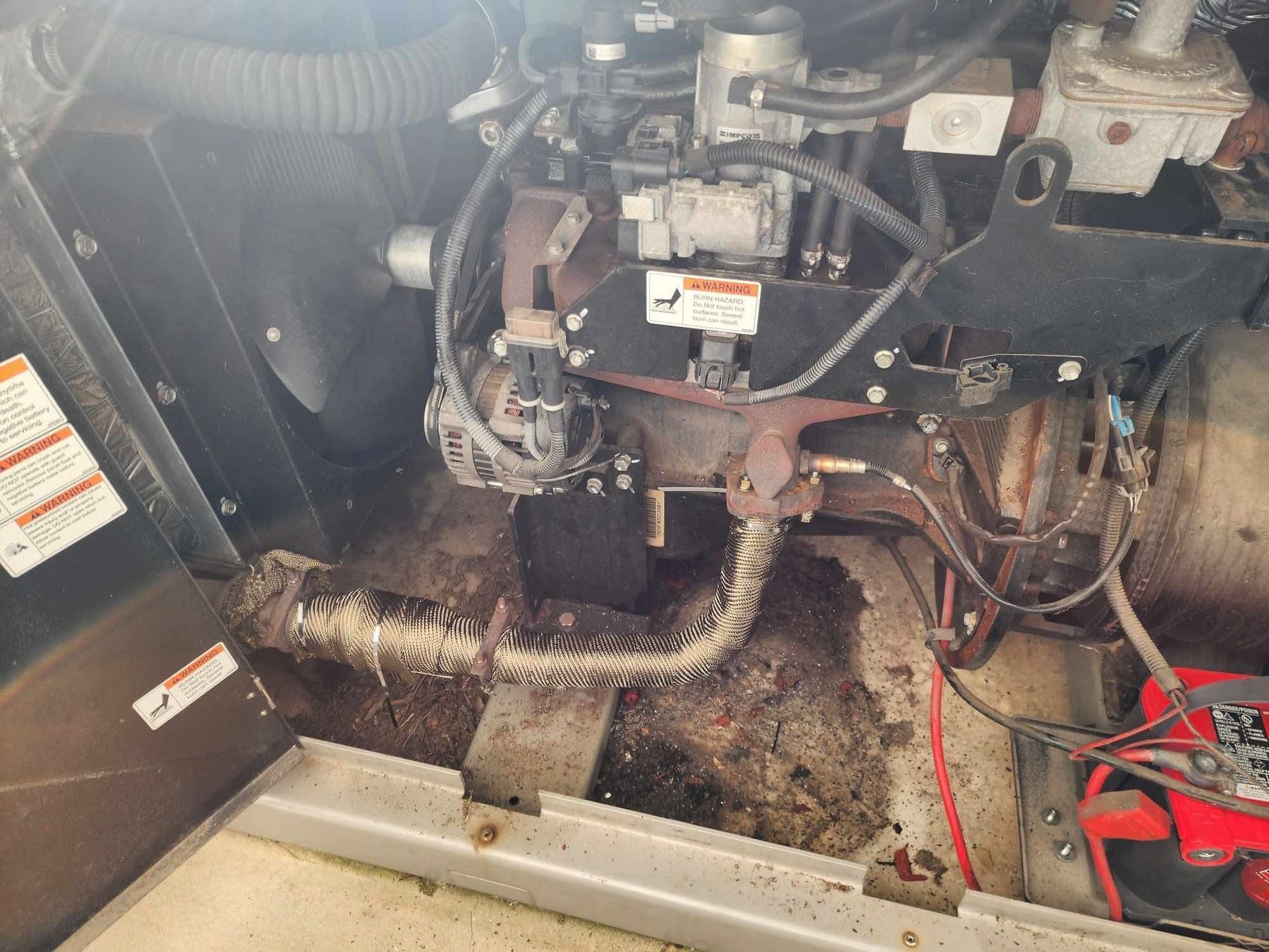 Dirty mechanical compartment with hoses, wiring, and a black box on a dusty floor panel