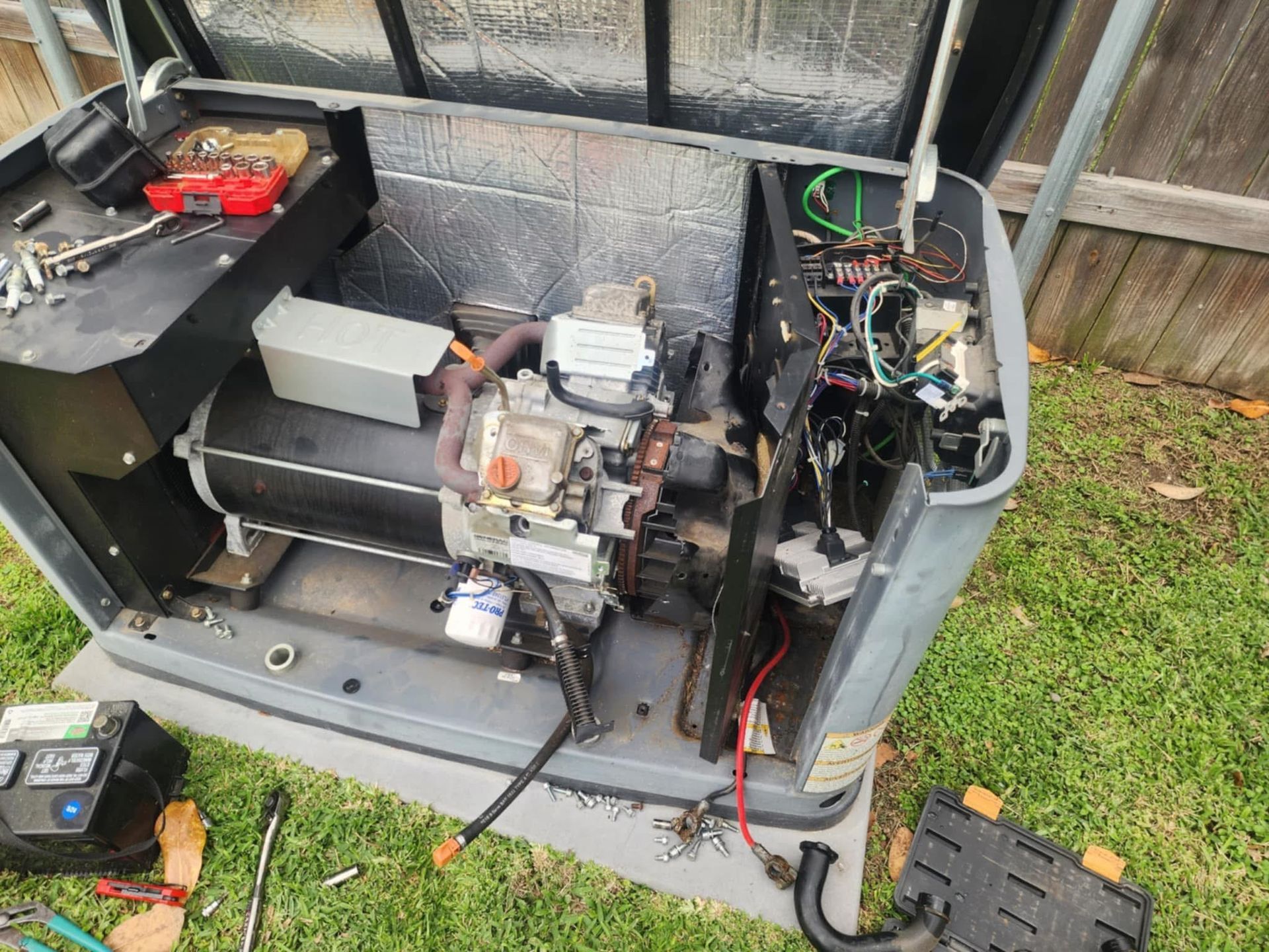 Open generator on grass, showing engine, wiring, and battery compartments.