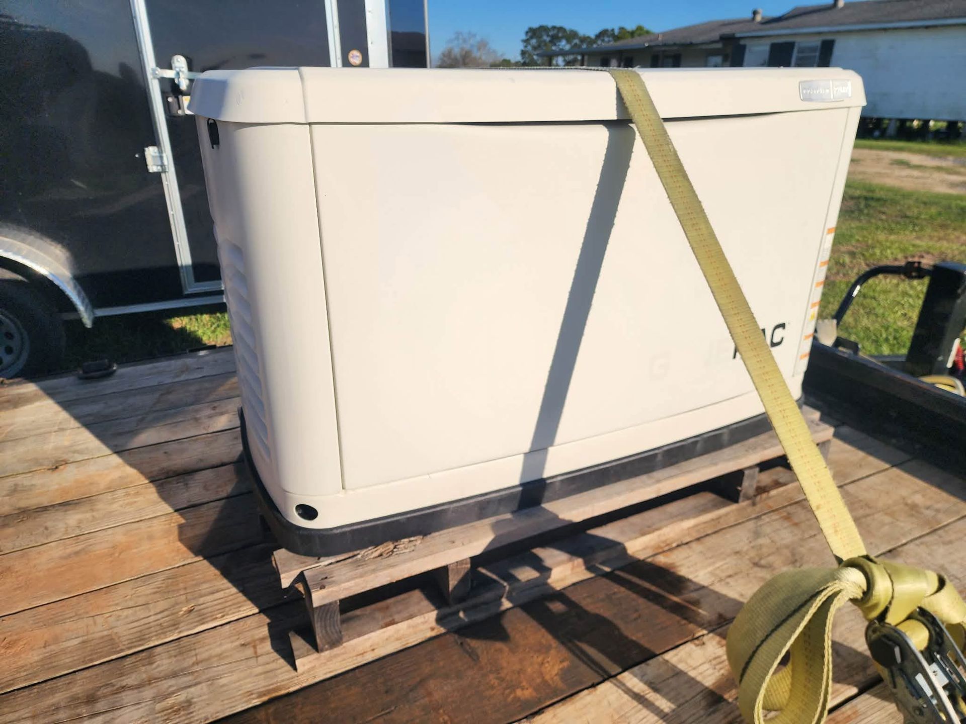 White hot tub strapped to a wooden pallet with a yellow ratchet strap outdoors in sunlight