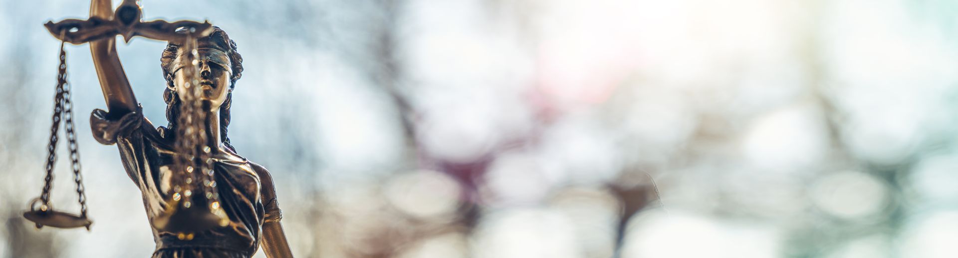 Statue of Lady Justice with scales against a softly blurred background.