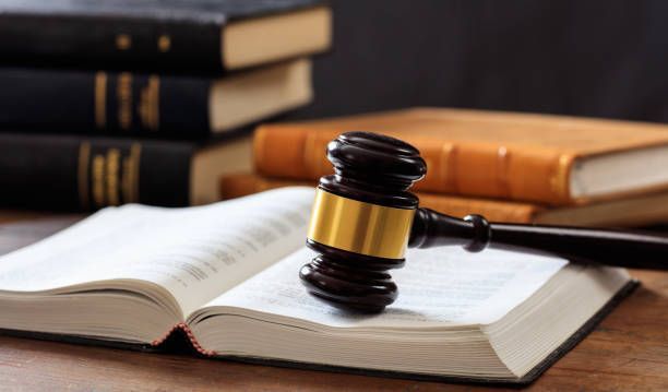 Gavel resting on open law book, with stack of books in background, representing legal context.