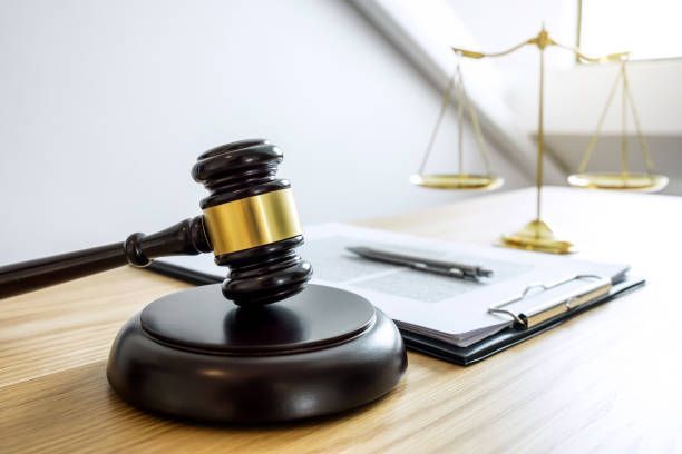 Gavel on a wooden block with a golden scale of justice, a pen, and document on a clipboard in the background.