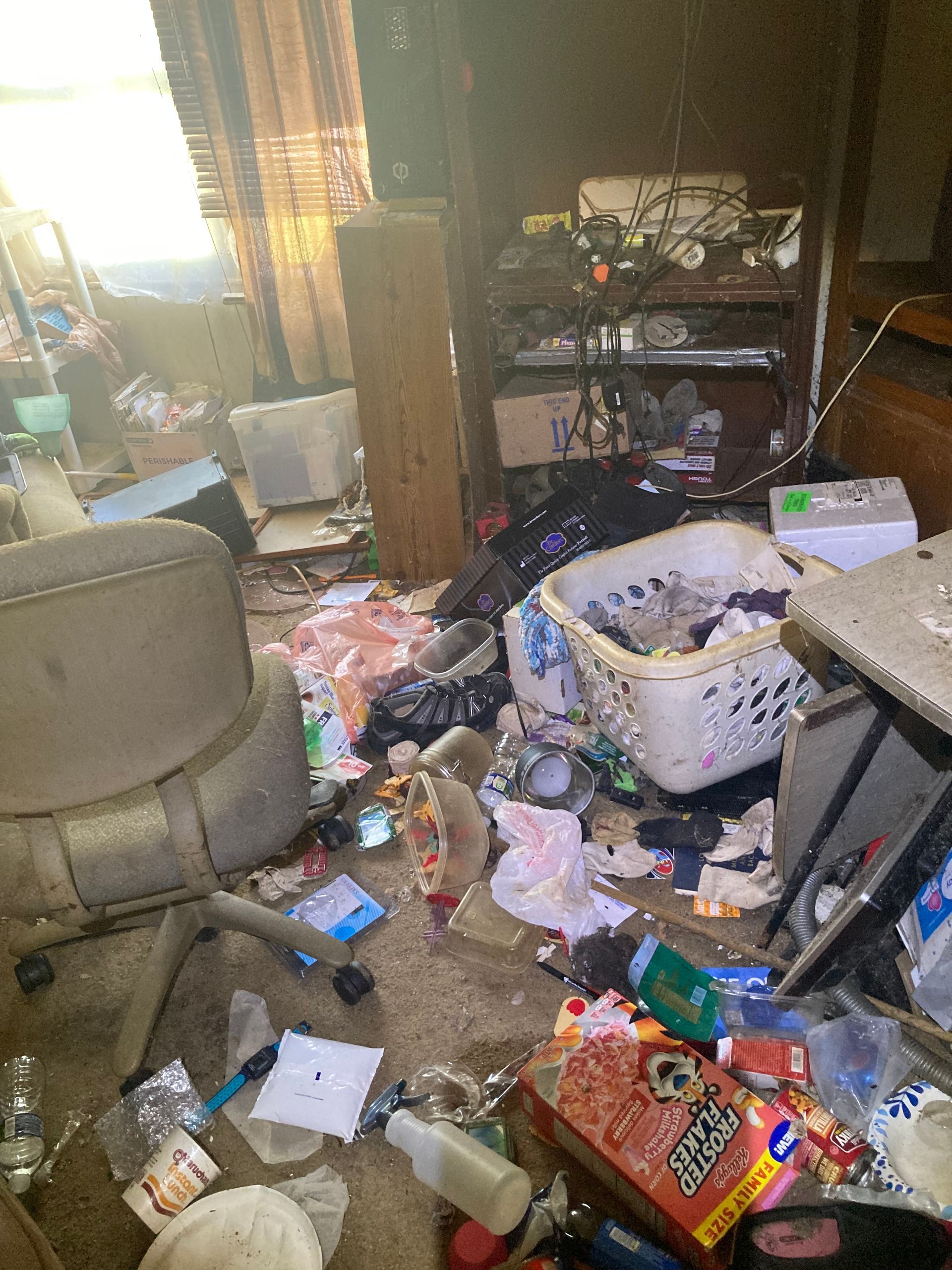 A cluttered room with trash, old furniture, and an unorganized shelf.