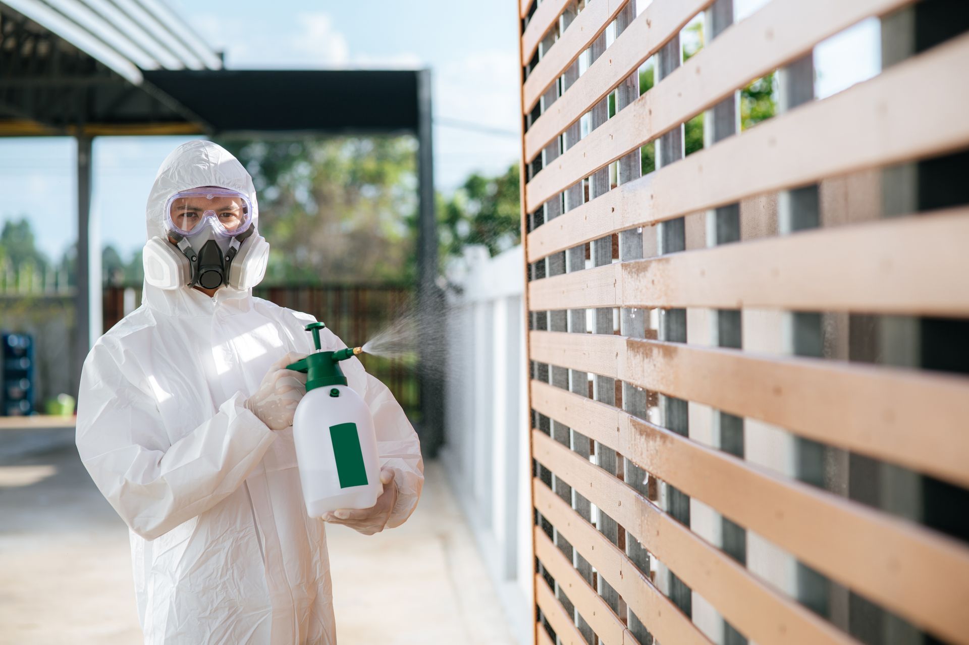 A man in a protective suit is spraying a wall with a spray bottle.