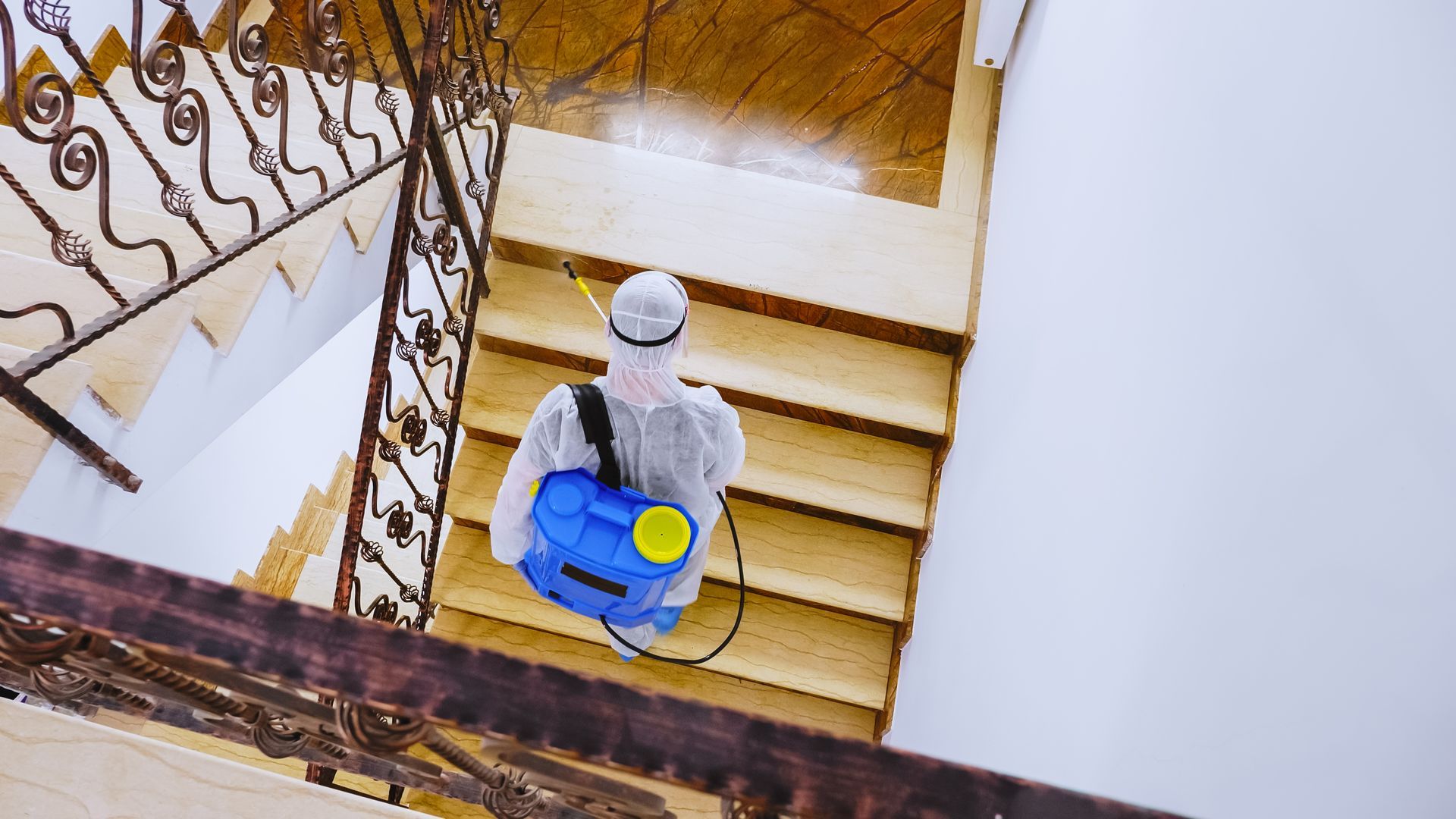A man in a protective suit is spraying disinfectant on a set of stairs.