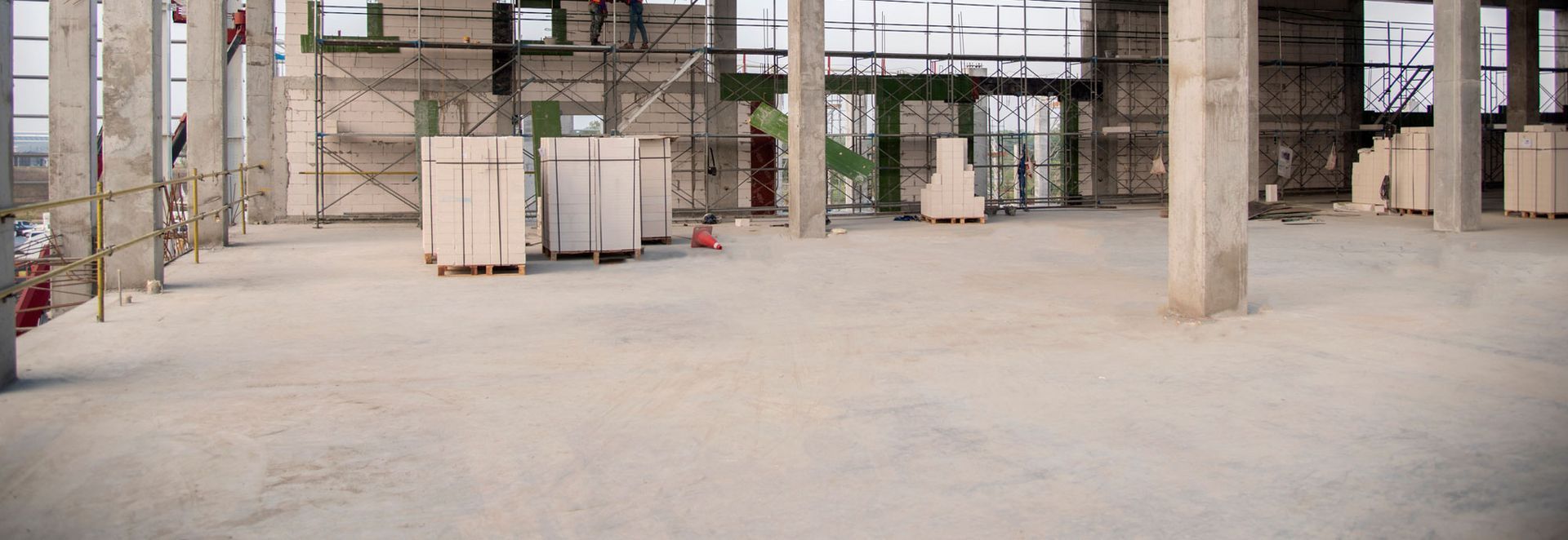 A large empty building under construction with scaffolding and boxes on the floor.