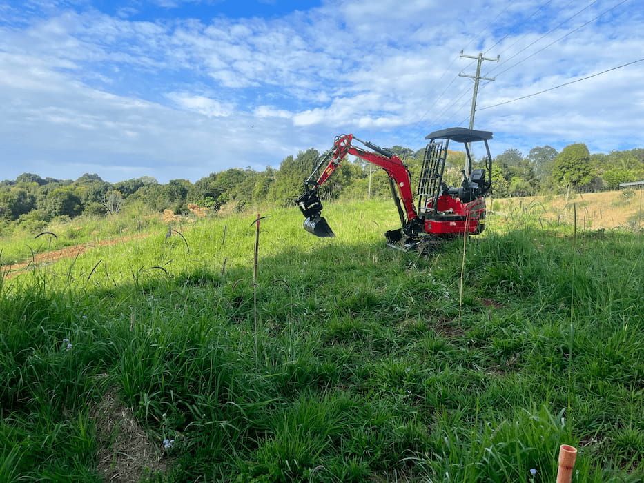 A Small Red Excavator Is Sitting in The Middle of A Grassy Field — ZBM Constructions in Alstonville, NSW