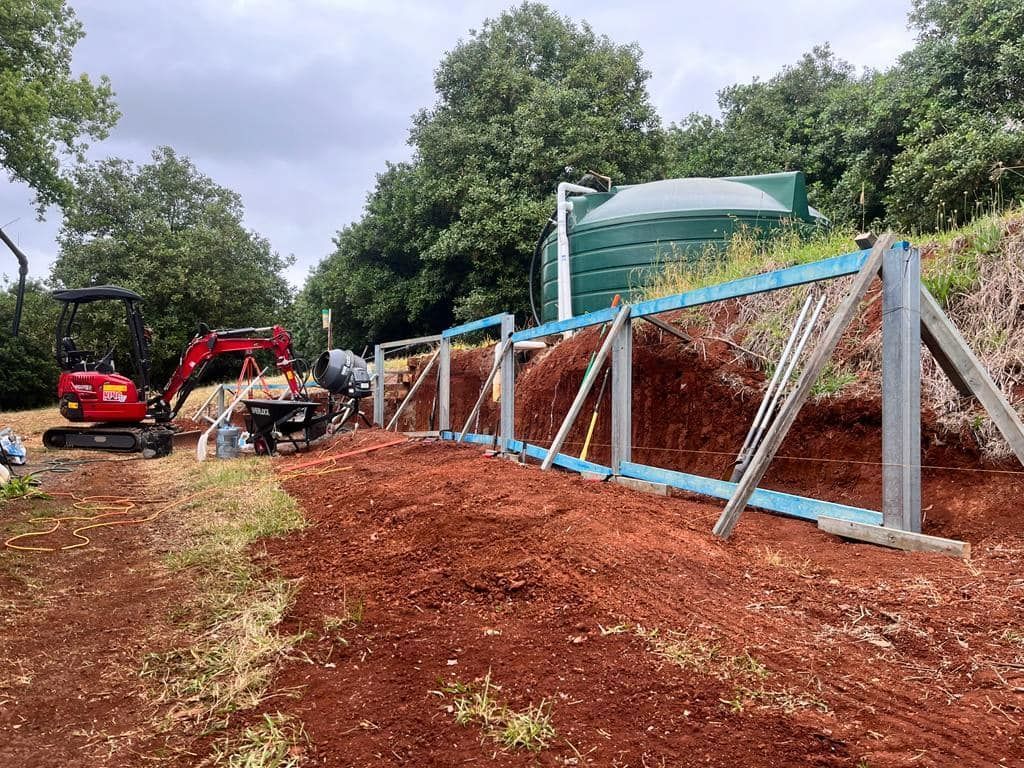A Red Excavator Is Working on A Fence in A Dirt Field — ZBM Constructions in Ballina, NSW