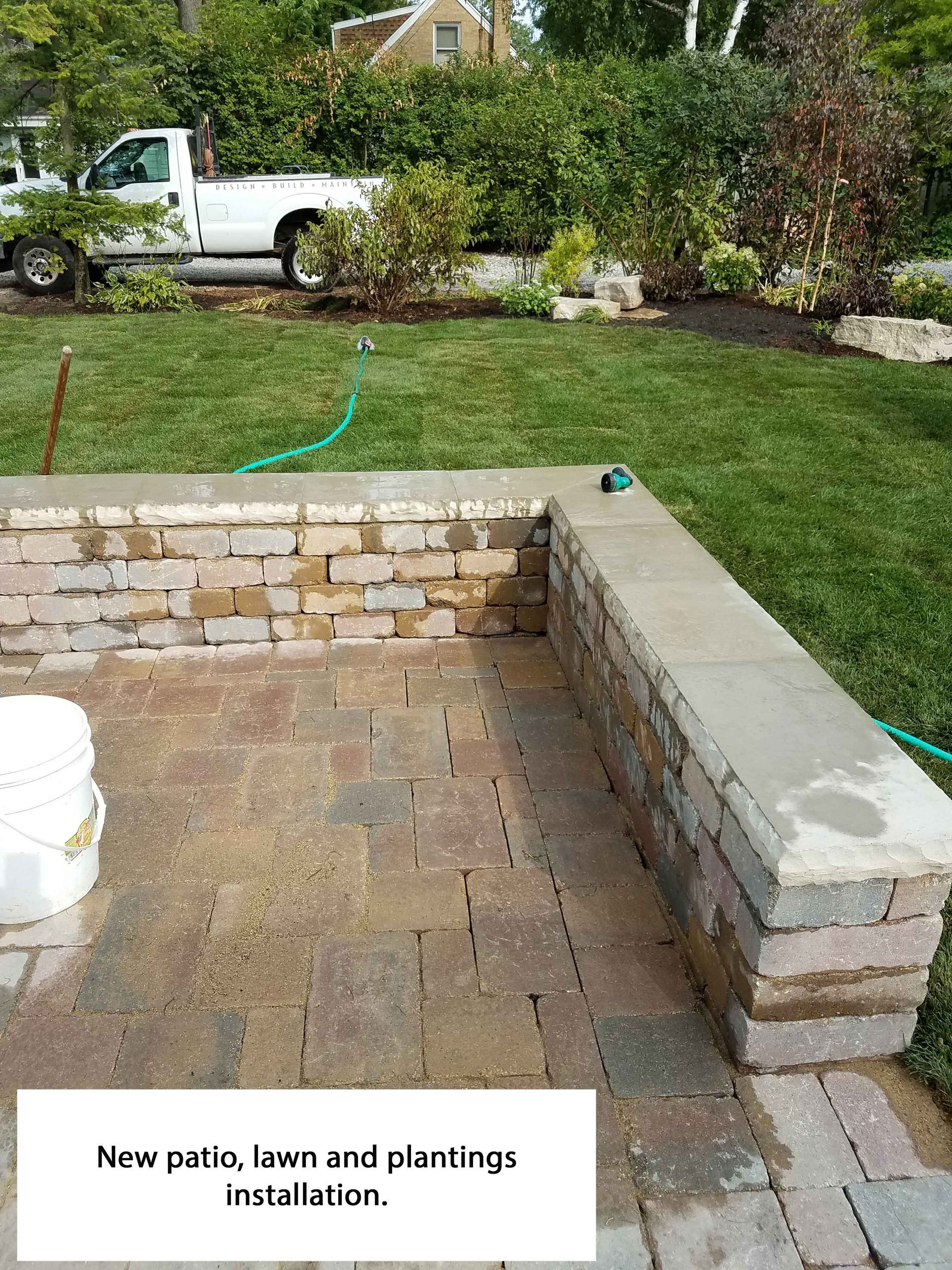 Patio with brick pavers, low wall, and green lawn; a truck is parked in the background.