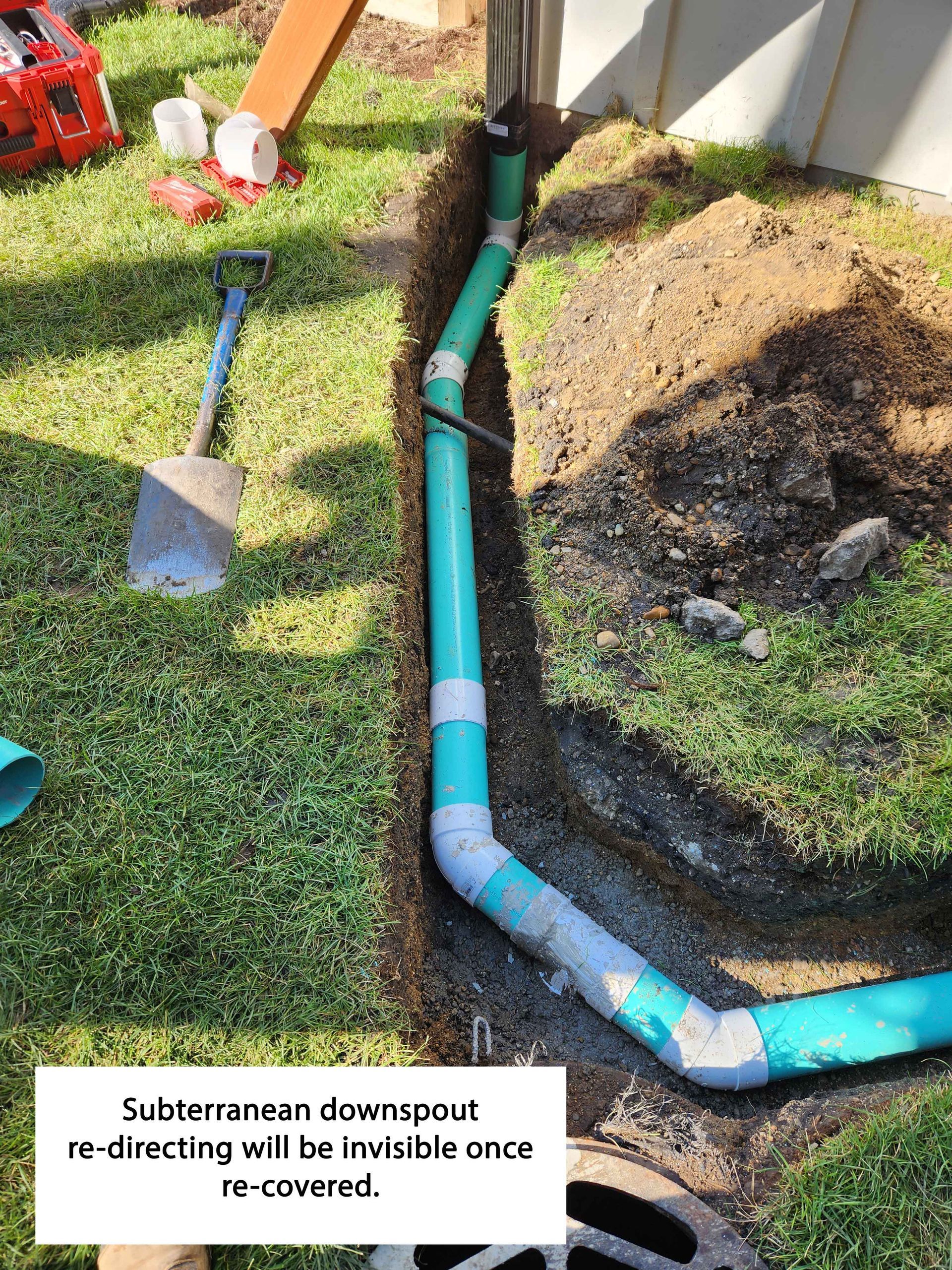 Green drain pipe installation in trench, running from a downspout toward a drain, on a grassy lawn.