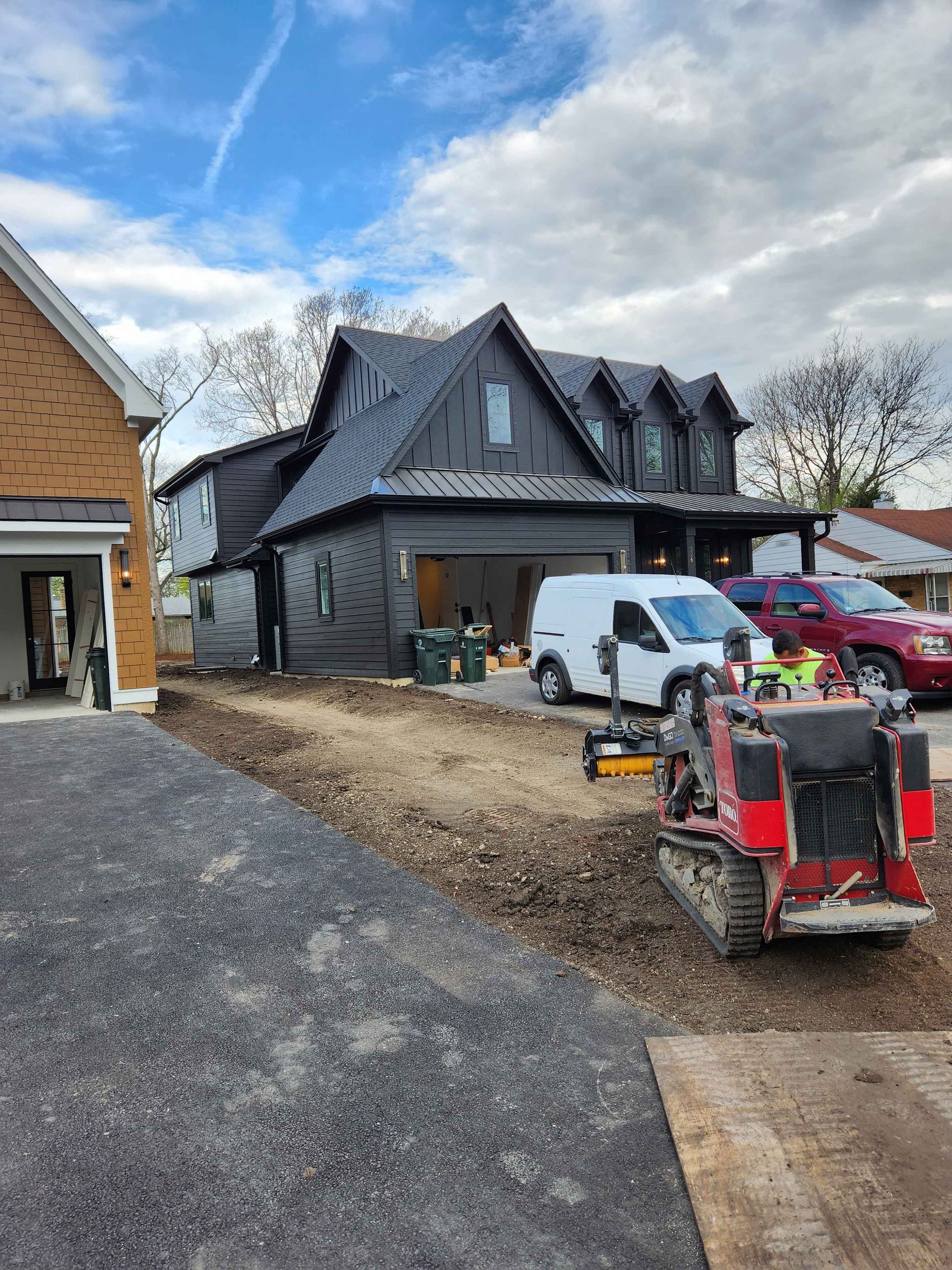 Black house under construction with driveway, work truck, and machinery in front.