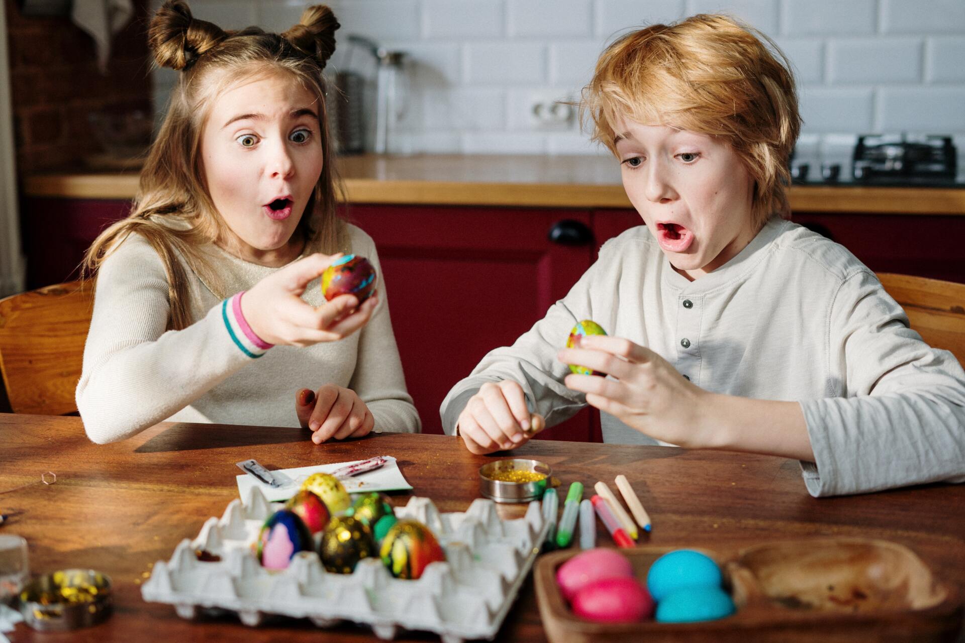Un niño y una niña están sentados en una mesa decorando huevos de Pascua.