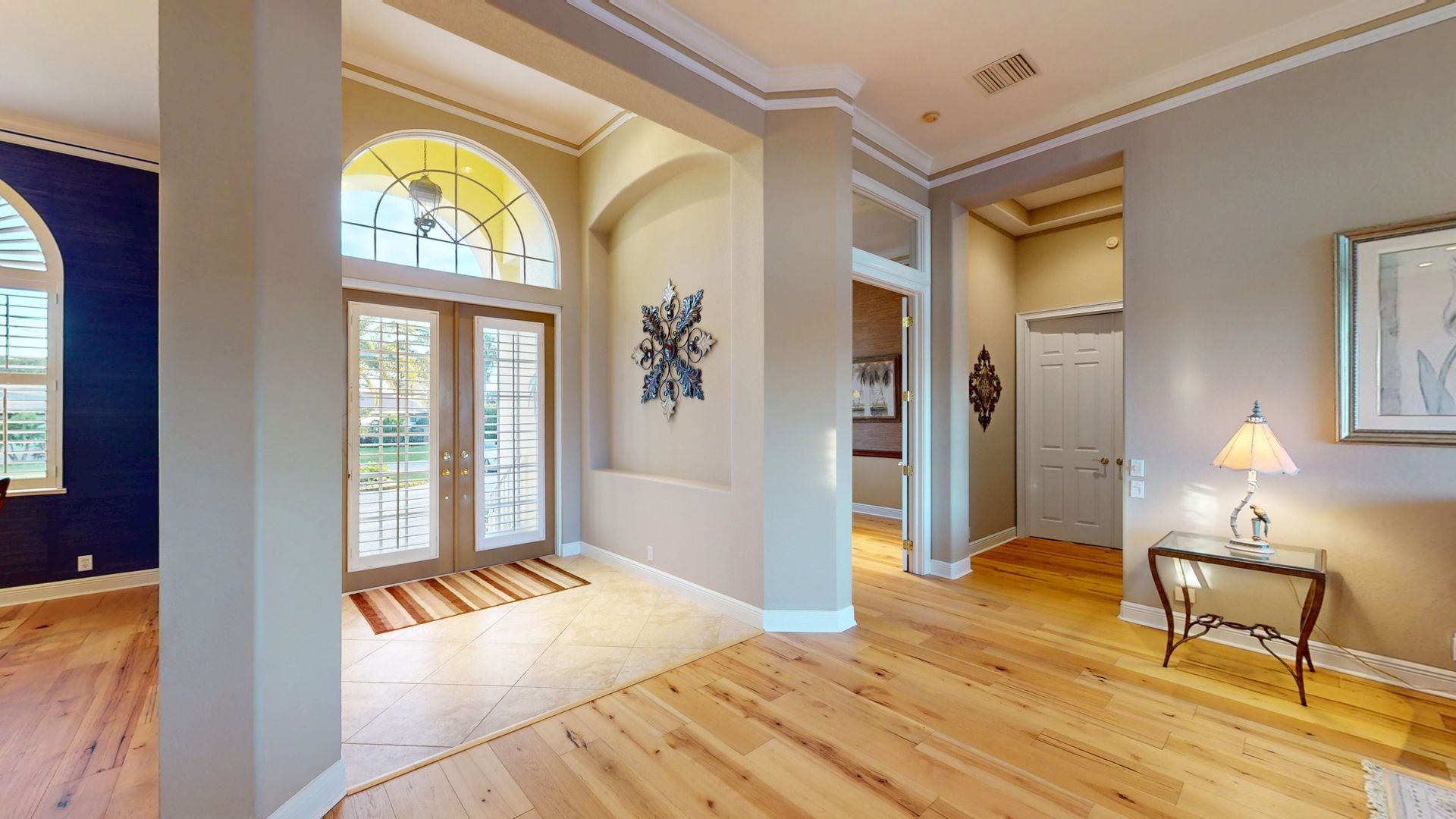 A brightly lit, upscale living room with hardwood floors, comfortable seating, and large glass doors leading to an outdoor patio with water views.