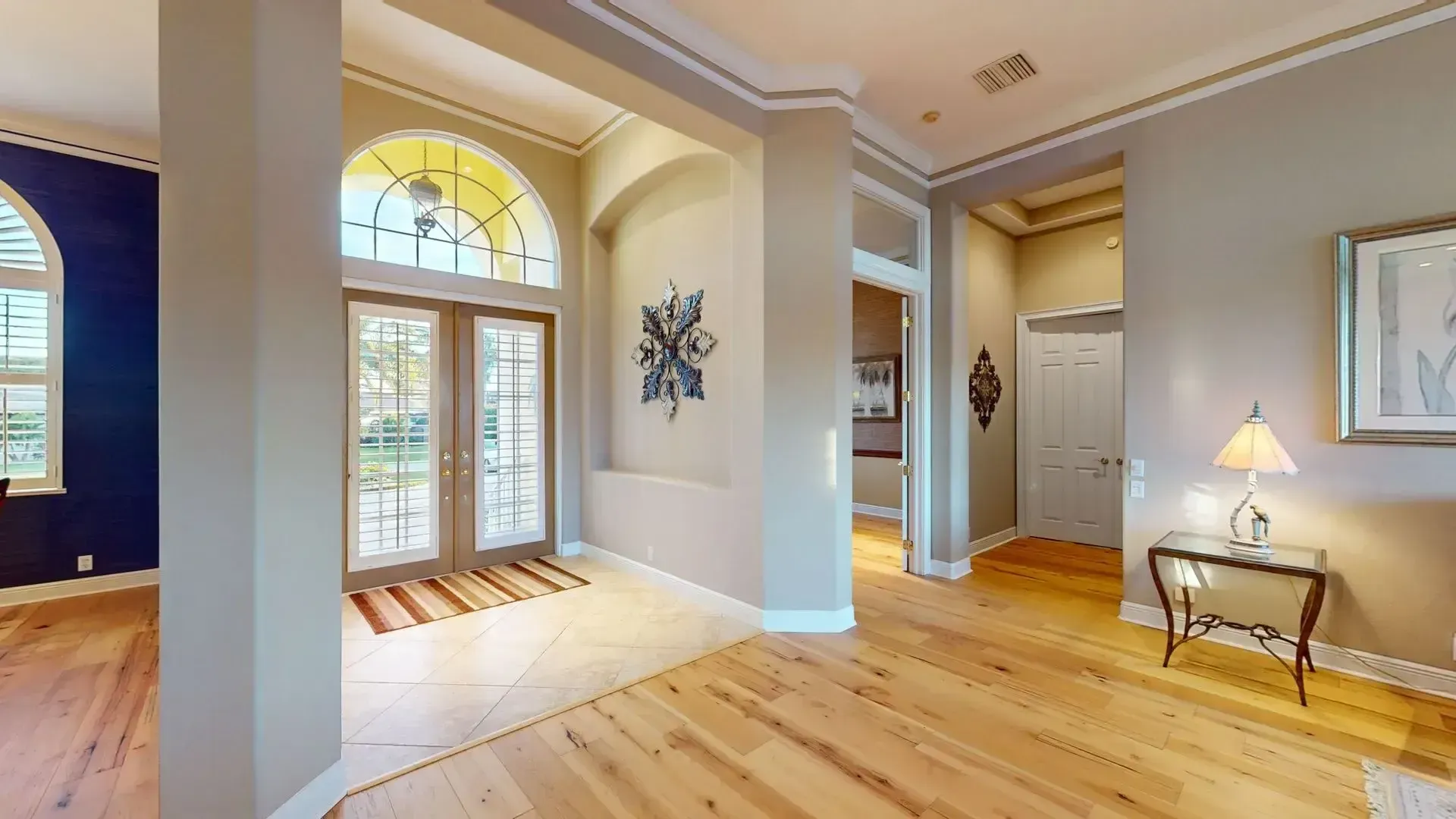 A brightly lit, upscale living room with hardwood floors, comfortable seating, and large glass doors leading to an outdoor patio with water views.