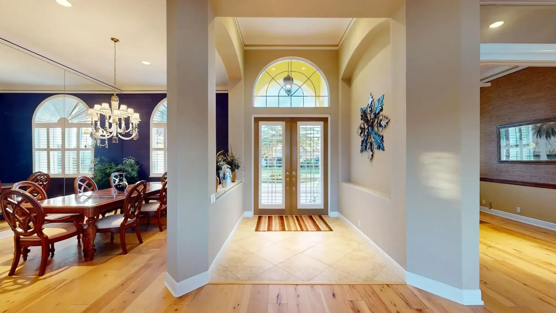 A brightly lit, upscale living room with hardwood floors, comfortable seating, and large glass doors leading to an outdoor patio with water views.