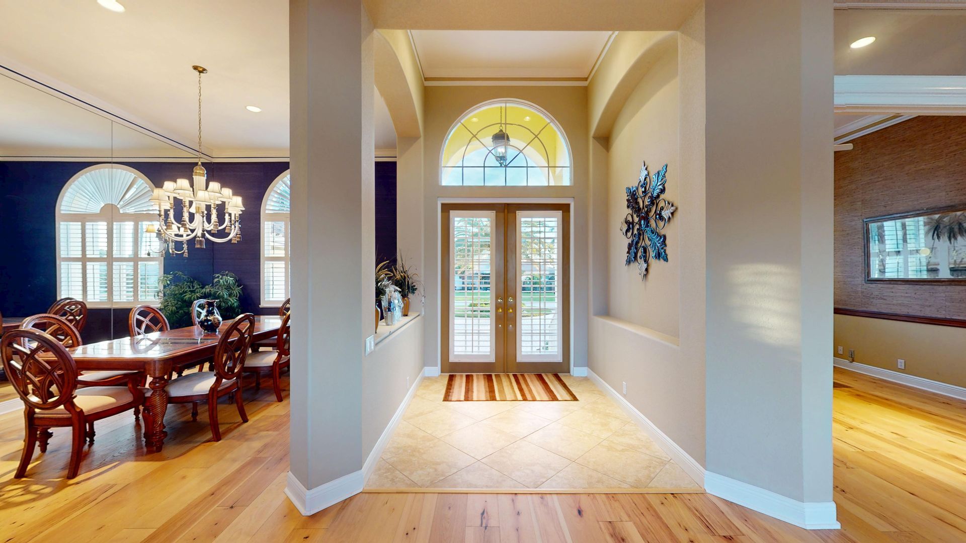 A brightly lit, upscale living room with hardwood floors, comfortable seating, and large glass doors leading to an outdoor patio with water views.