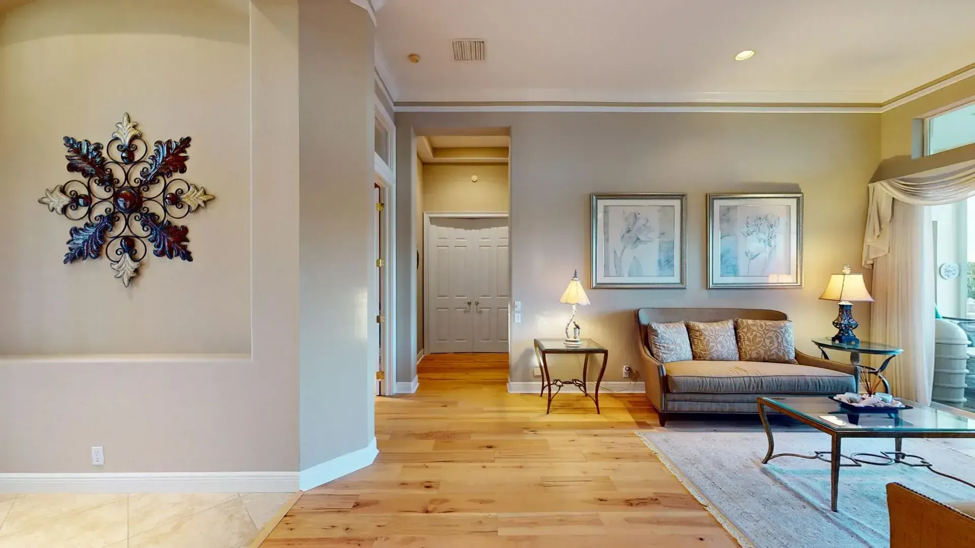Spacious living room with light hardwood floors, high ceilings, a tan sofa and armchair, and large glass sliding doors that open to a covered patio with a waterfront view.