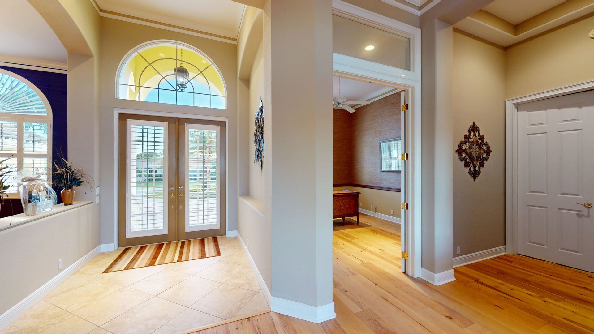 A brightly lit, upscale living room with hardwood floors, comfortable seating, and large glass doors leading to an outdoor patio with water views.