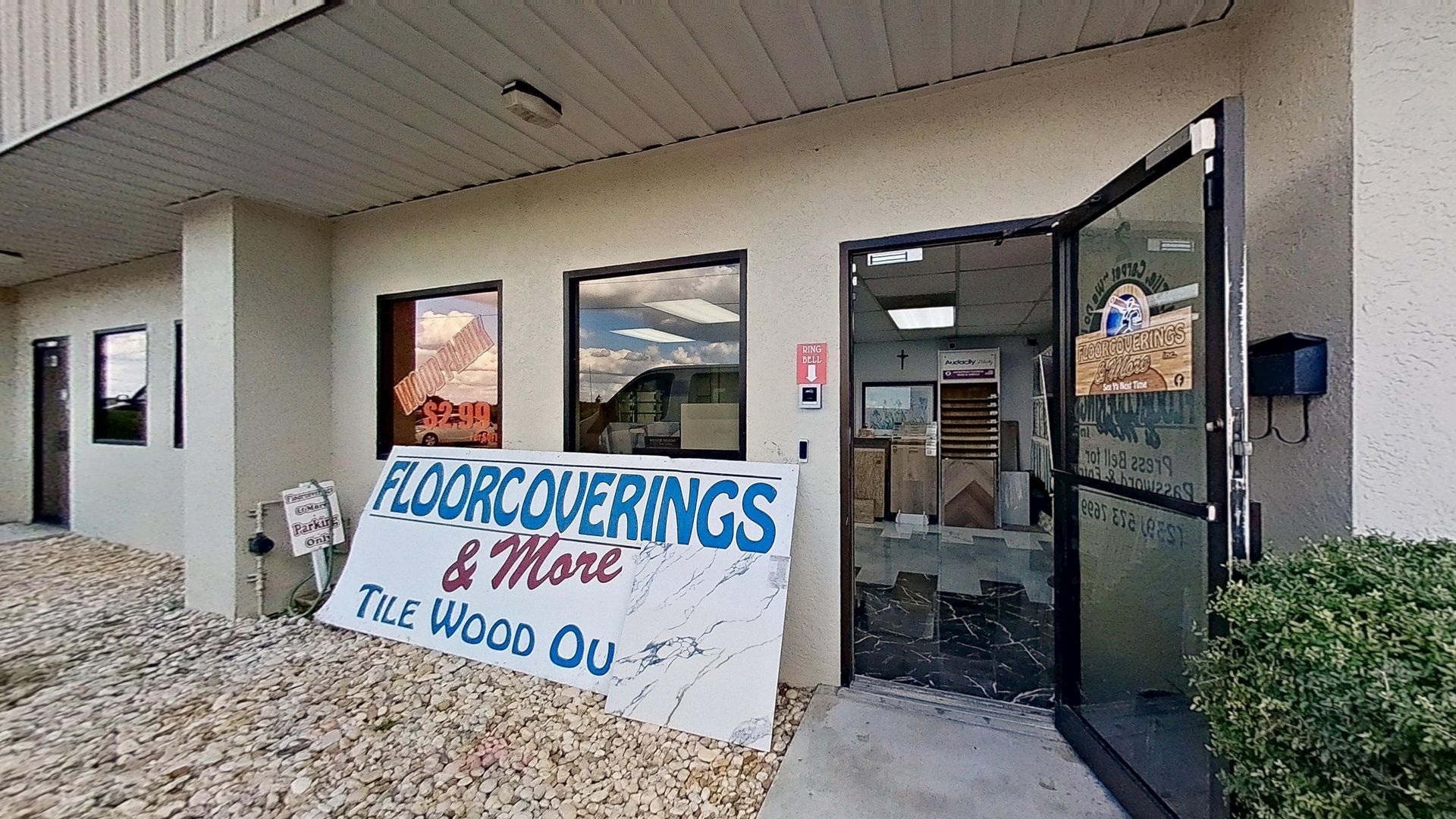 The front entrance of Floorcoverings & More Inc., featuring large signage outside, a glass door with a logo, and a view into the tile and flooring showroom.