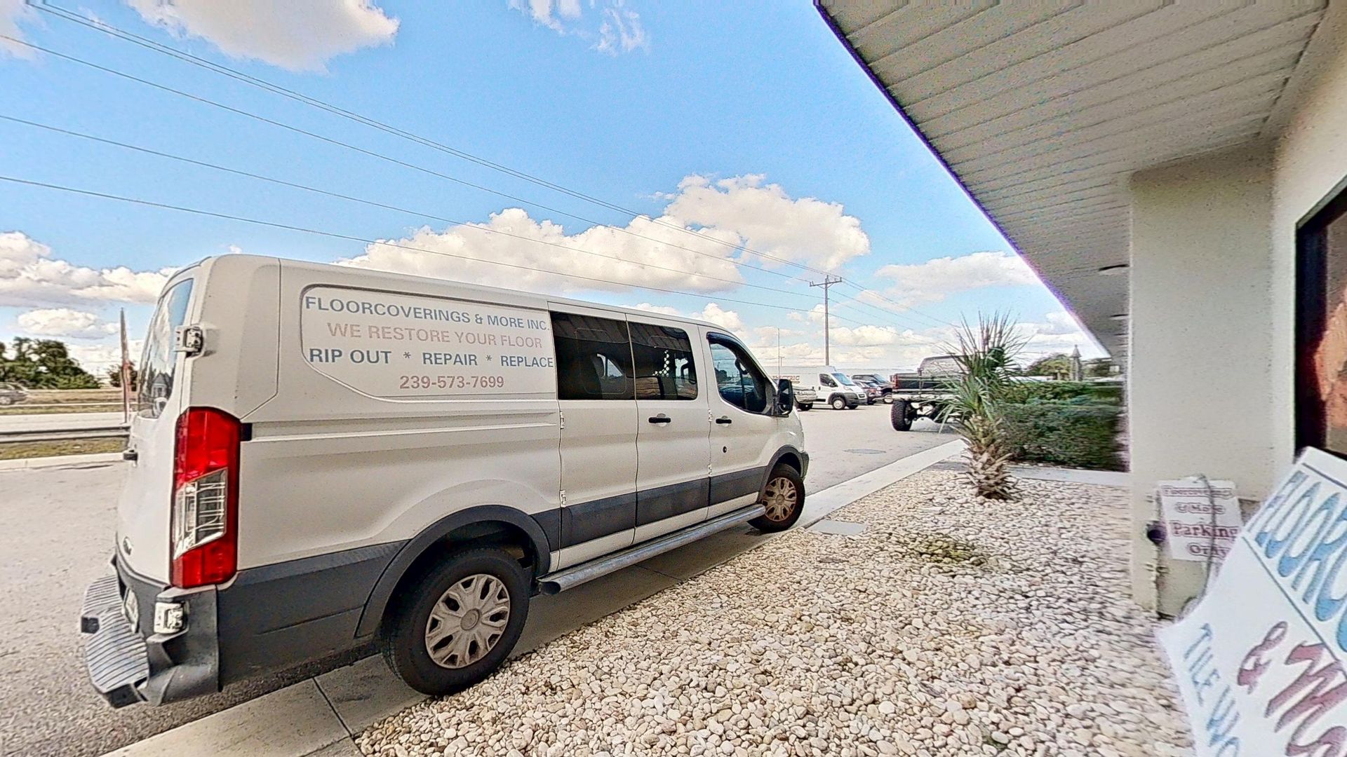 A white commercial service van parked outside a store, with text on the side reading 'Floorcoverings & More Inc. We Restore Your Floor: Rip Out, Repair, Replace' alongside a phone number.