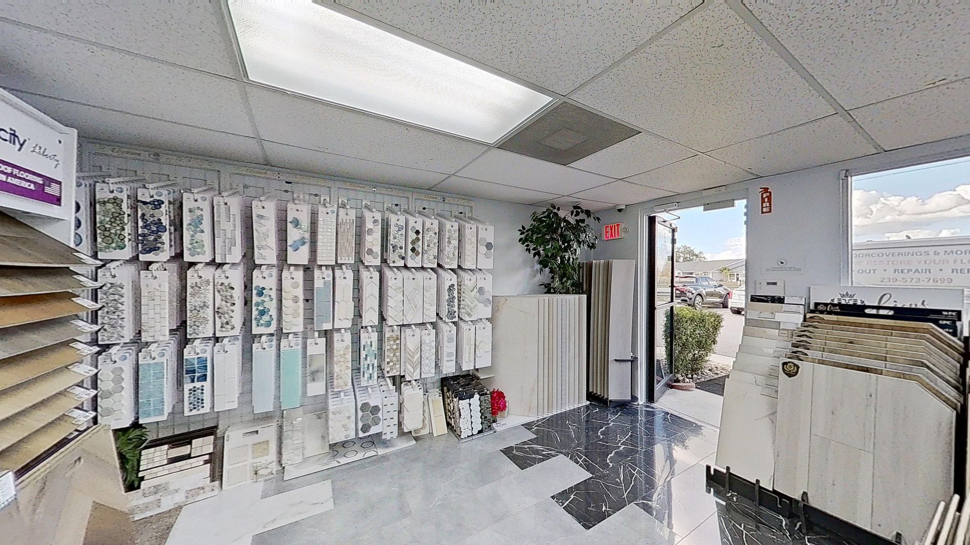 An indoor showroom wall displaying rows of hanging mosaic and tile samples in various geometric shapes, colors, and textures, next to an Audacity brand flooring display.