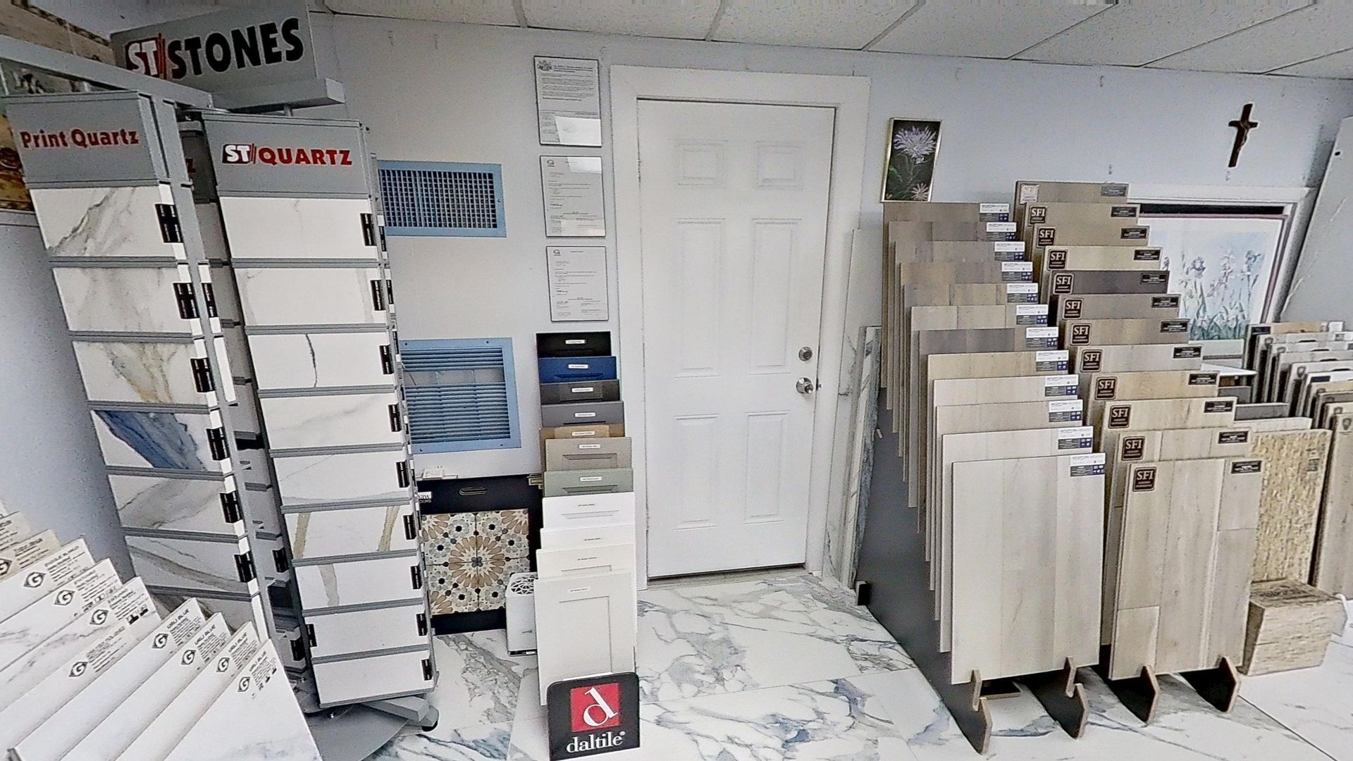 An indoor showroom wall displaying rows of hanging mosaic and tile samples in various geometric shapes, colors, and textures, next to an Audacity brand flooring display.