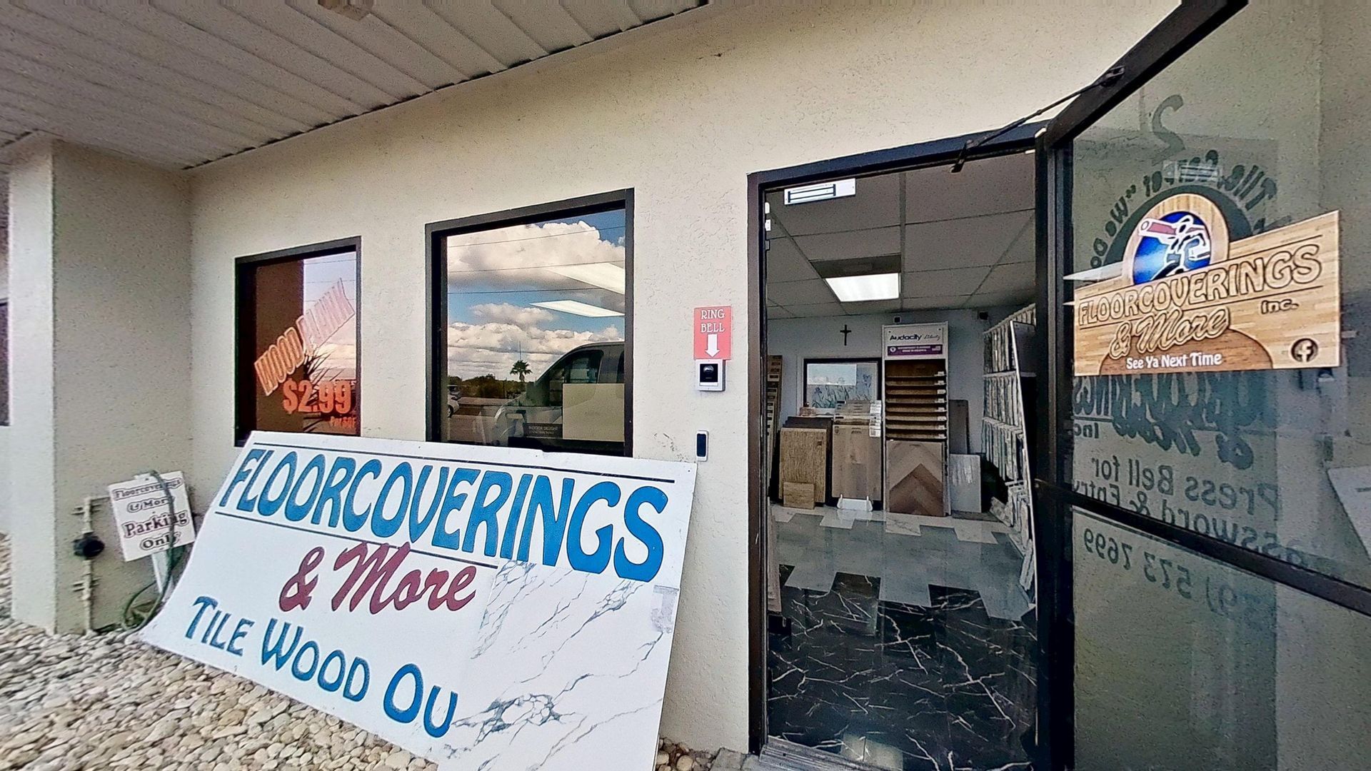 The front entrance of Floorcoverings & More Inc., featuring large signage outside, a glass door with a logo, and a view into the tile and flooring showroom.