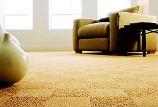 Tan carpet with a square pattern in a room with a beige armchair, small table, and windows.