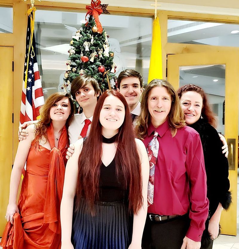 Group of six people posing in front of a Christmas tree and an American flag.