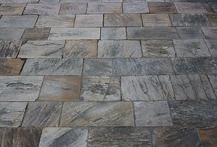 Close-up view of stone pavers in shades of gray, brown, and tan, arranged in a rectangular pattern.