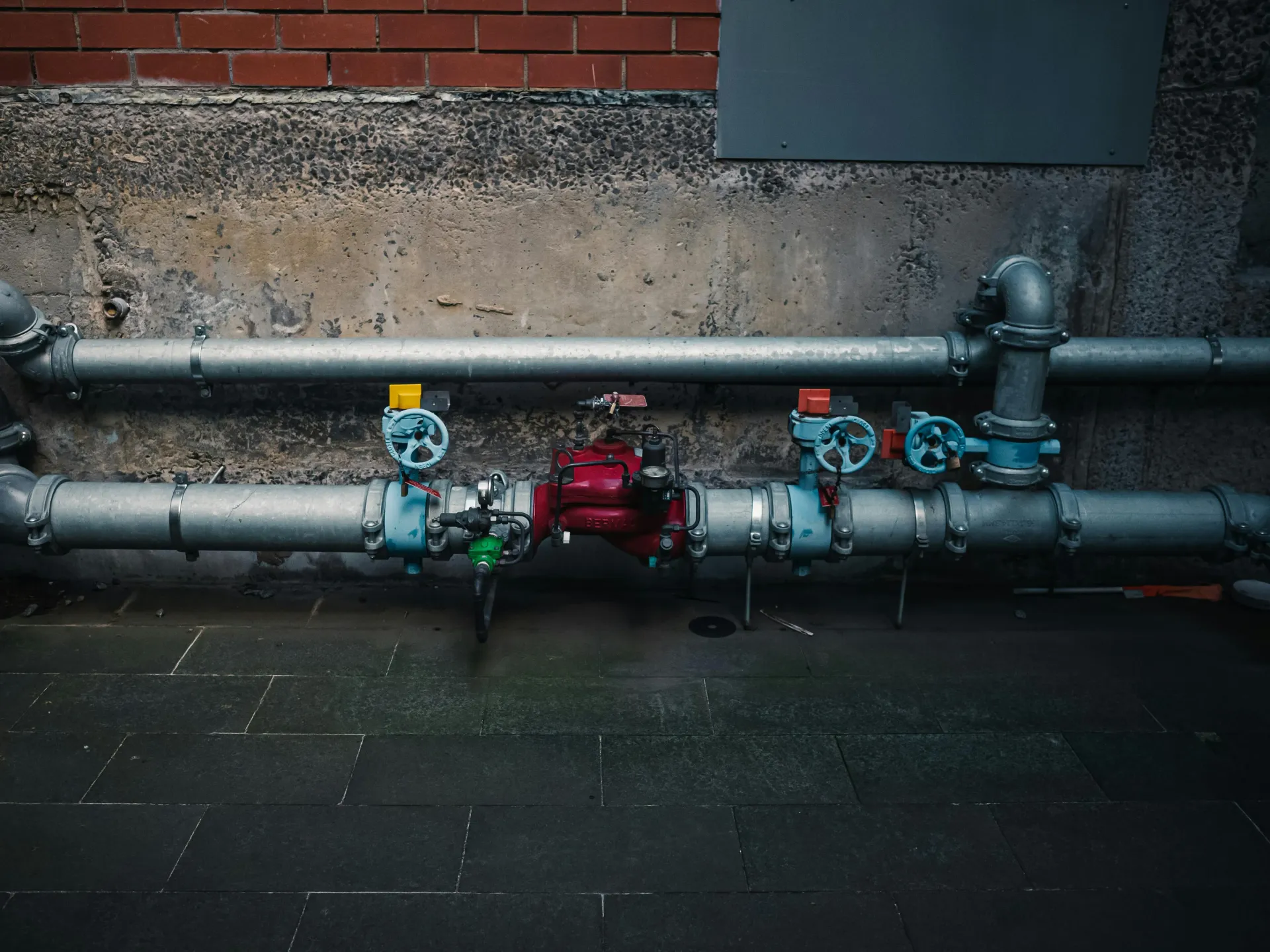 Outdoor industrial water pipes with colorful valves against a brick wall